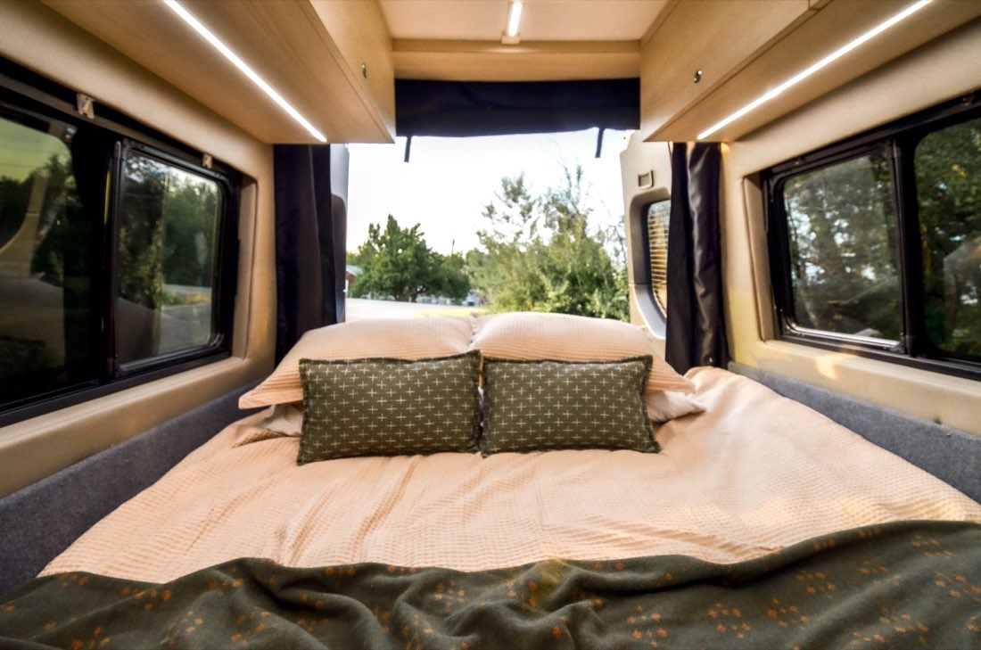 Made-up queen bed with the rear doors open to trees